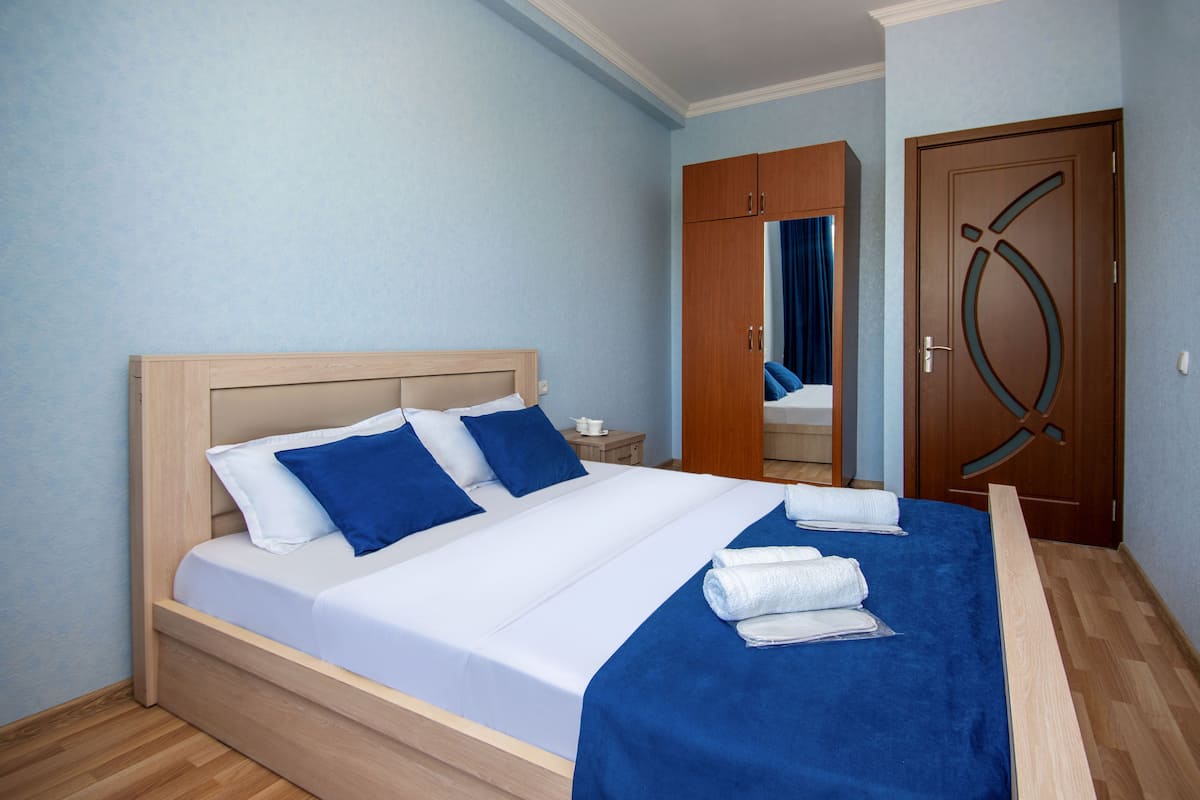 A neatly made bed with blue and white bedding, a wooden headboard, and a blue throw blanket.
