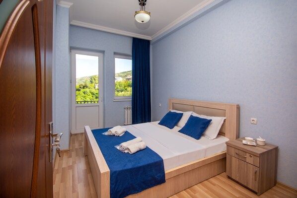A bedroom with a bed, a nightstand, a window, and a view of greenery outside.