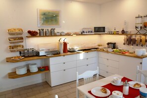 Una cocina moderna con armarios blancos, microondas, tostadora y diversos productos para el desayuno en estantes.