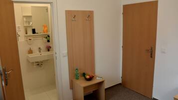 A bathroom with a sink, mirror, and shelves with toiletries. There is a wooden bench with a bottle and fruit.