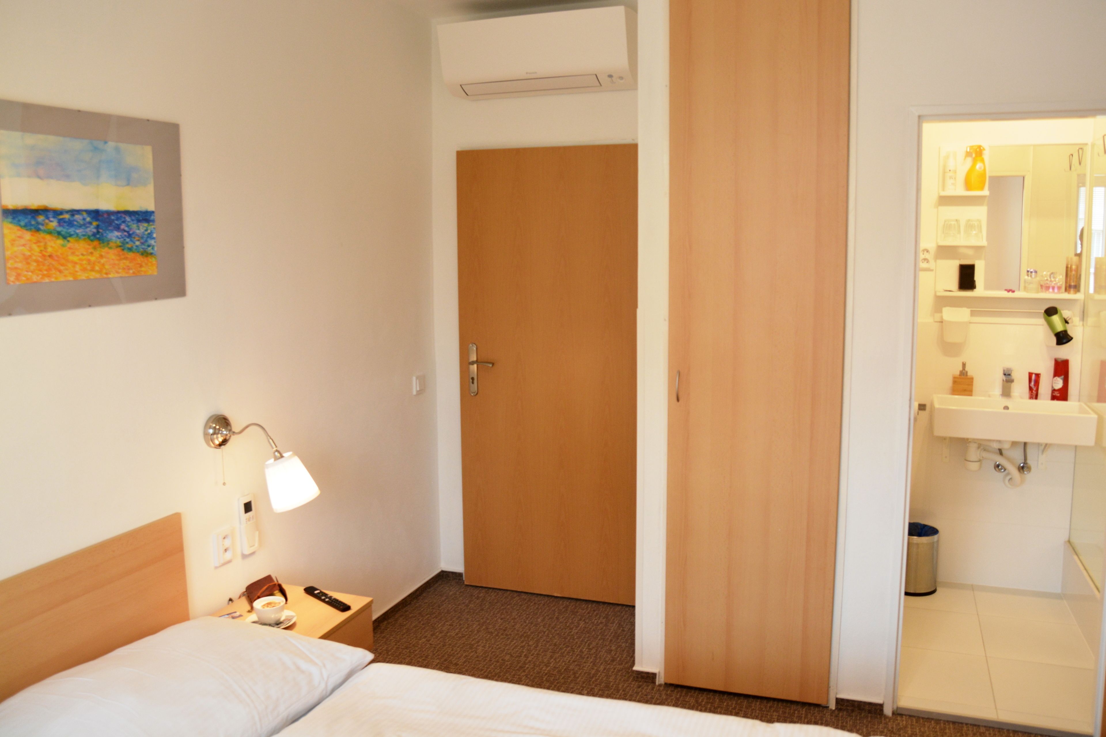Ett hotellrum med en säng, ett nattduksbord, en lampa och en tavla på väggen.