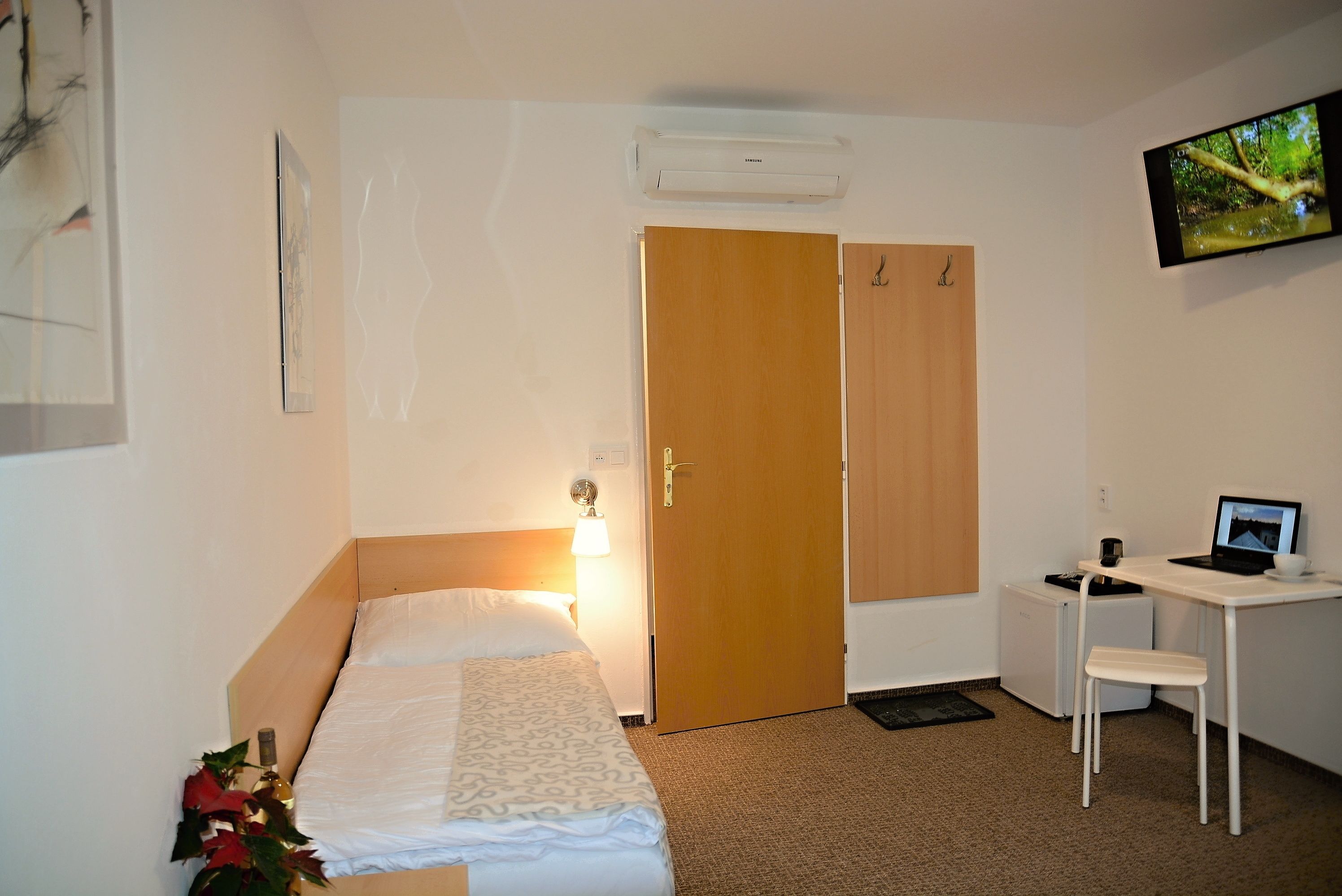 A hotel room with a bed, a desk with a computer, a TV, and a wardrobe.
