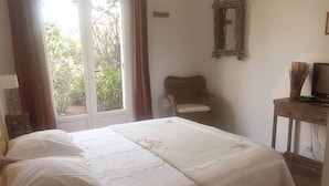 A bedroom with a bed, a chair, a television, and a window with curtains.