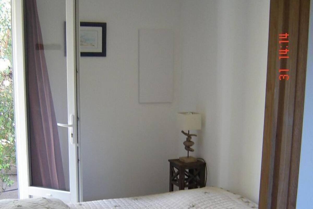 A bedroom with a bed, a small bedside table with a lamp, a door, and a framed picture on the wall.