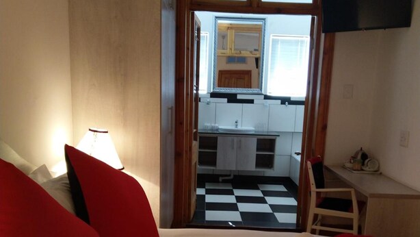 A hotel room with a bed, a desk, a chair, a TV, and a view of a kitchen. - Savoy Hotel Beaufort-West (Beaufort West)
