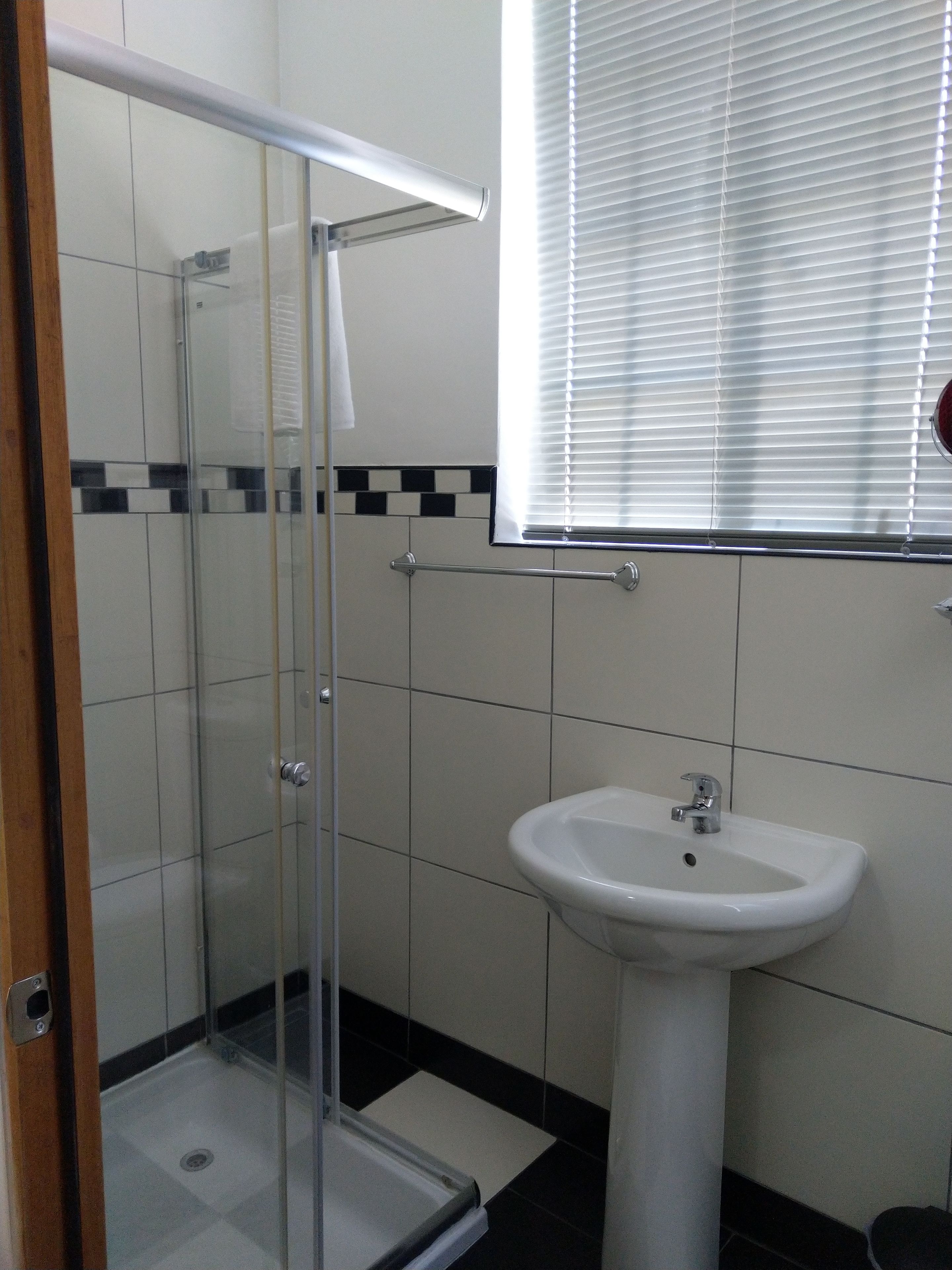 A bathroom with a glass shower enclosure, a white sink, and a window with blinds.