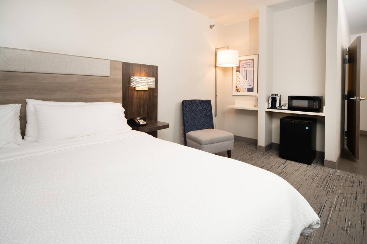 Habitación de hotel con una cama grande, una mesita de noche con teléfono, una silla, microondas y un refrigerador pequeño.