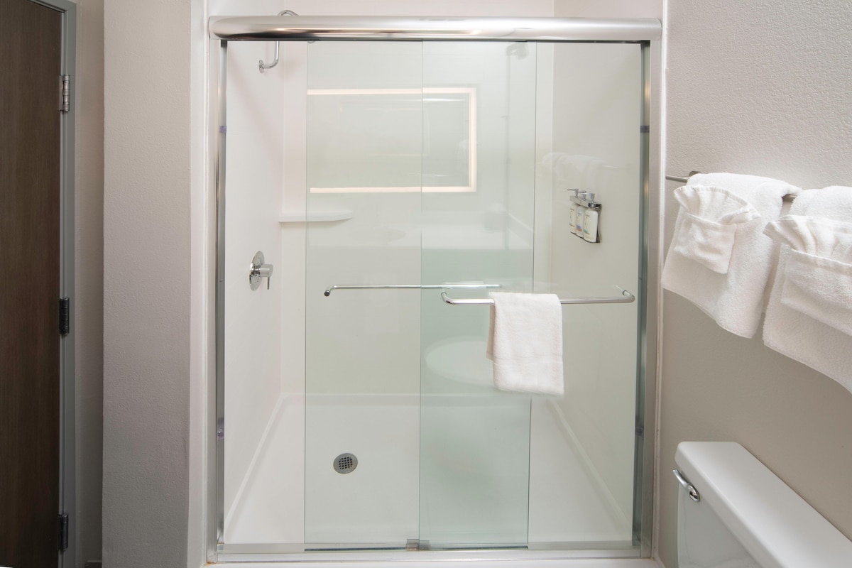A glass-enclosed shower stall with a towel rack and a toilet visible to the right.