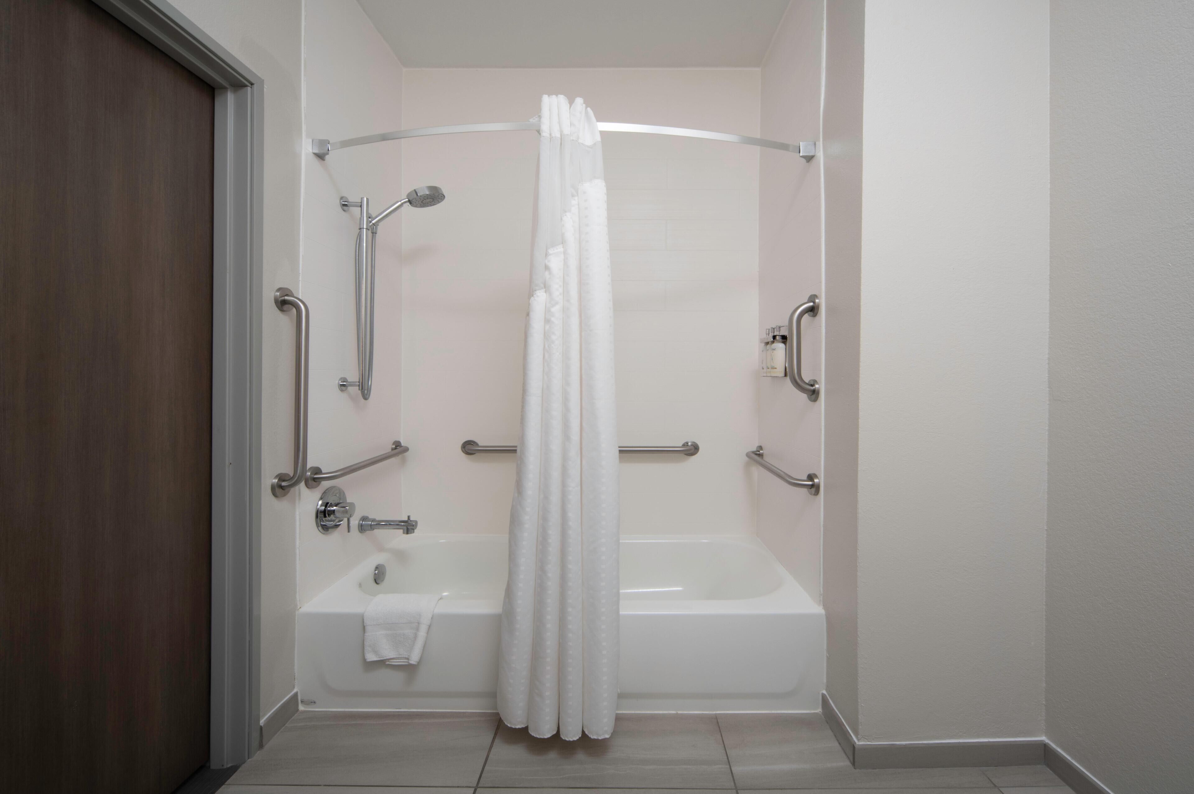 A bathroom with a bathtub, shower, and handrails.