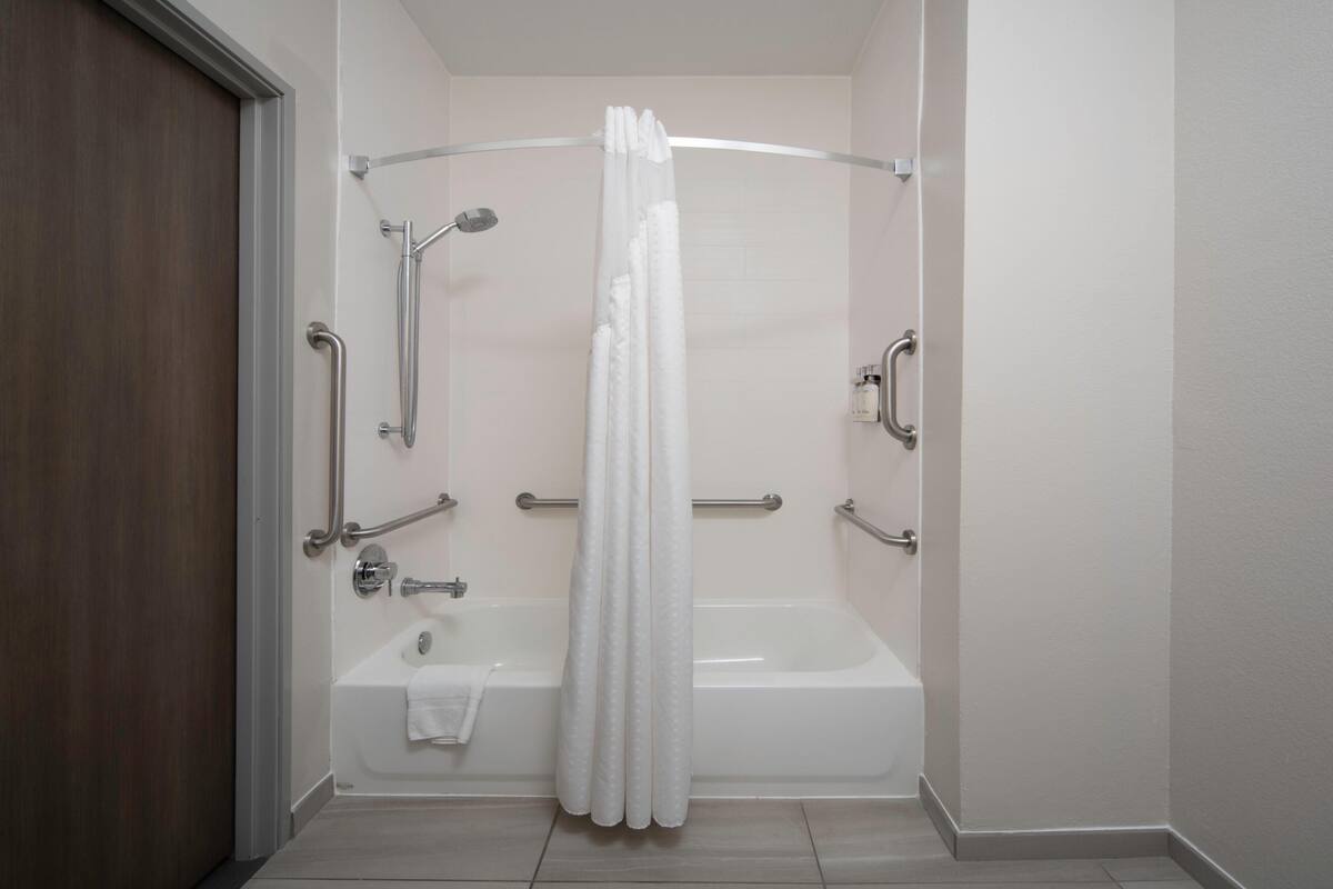 Un baño con bañera, ducha y barras de apoyo.