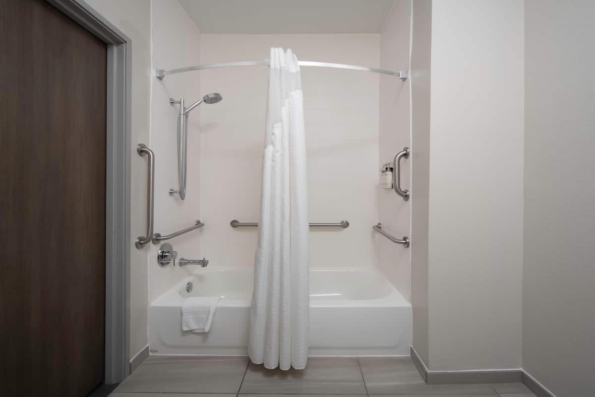 A bathroom with a bathtub, shower, and handrails.