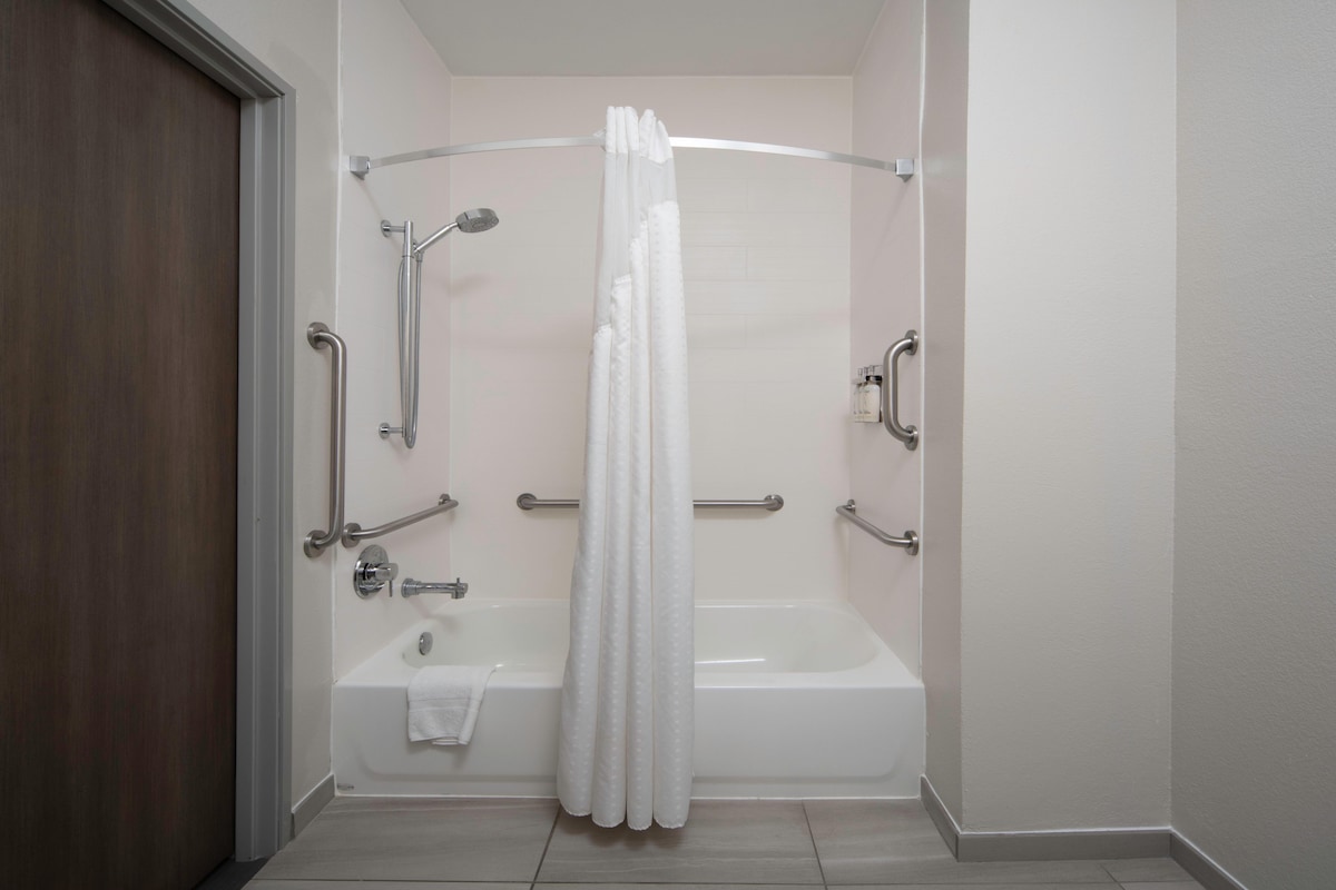 A bathroom with a bathtub, shower, and handrails.