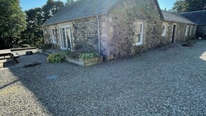A stone building with a sloped roof, a gravel driveway, and a clear sky. - Cottage for 6 in stunning rural location (Beech) (Crawfordjohn)