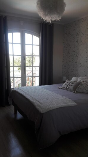 Relax in this serene bedroom with a large bed and a window with flowing curtains.