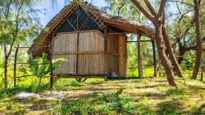 A rustic wooden structure with a thatched roof, surrounded by trees and greenery. - Varatraza Wind Riders (Antsiranana)