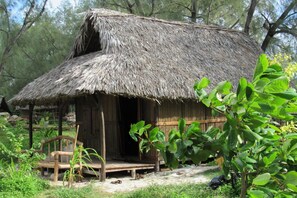 A rustic hut with a thatched roof, wooden walls, and a porch with a bench. - Varatraza Wind Riders (Antsiranana)