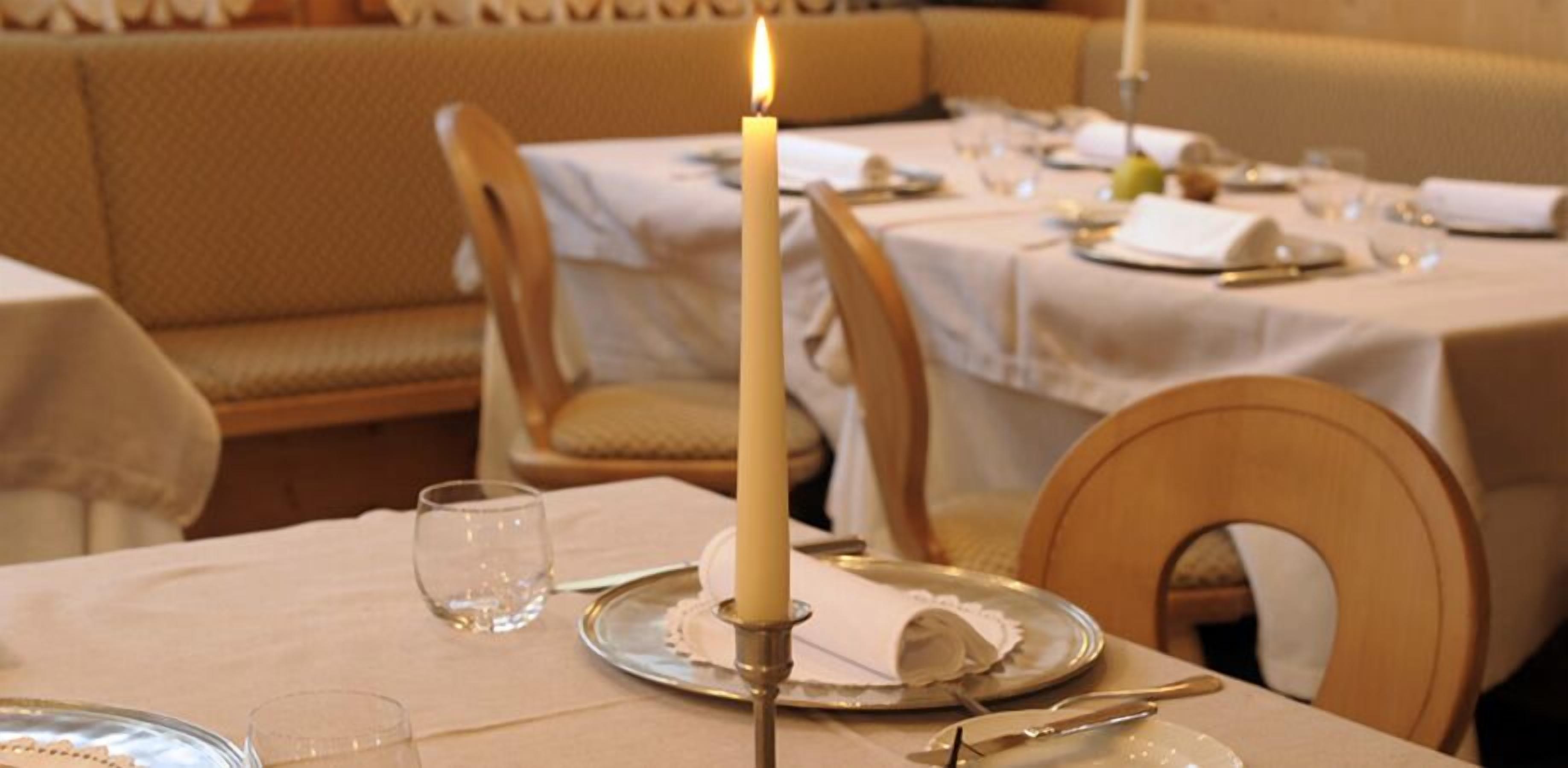 A dining table with a lit candle, a glass, and a plate with a napkin.