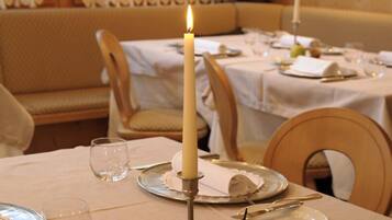 A dining table with a lit candle, a glass, and a plate with a napkin.