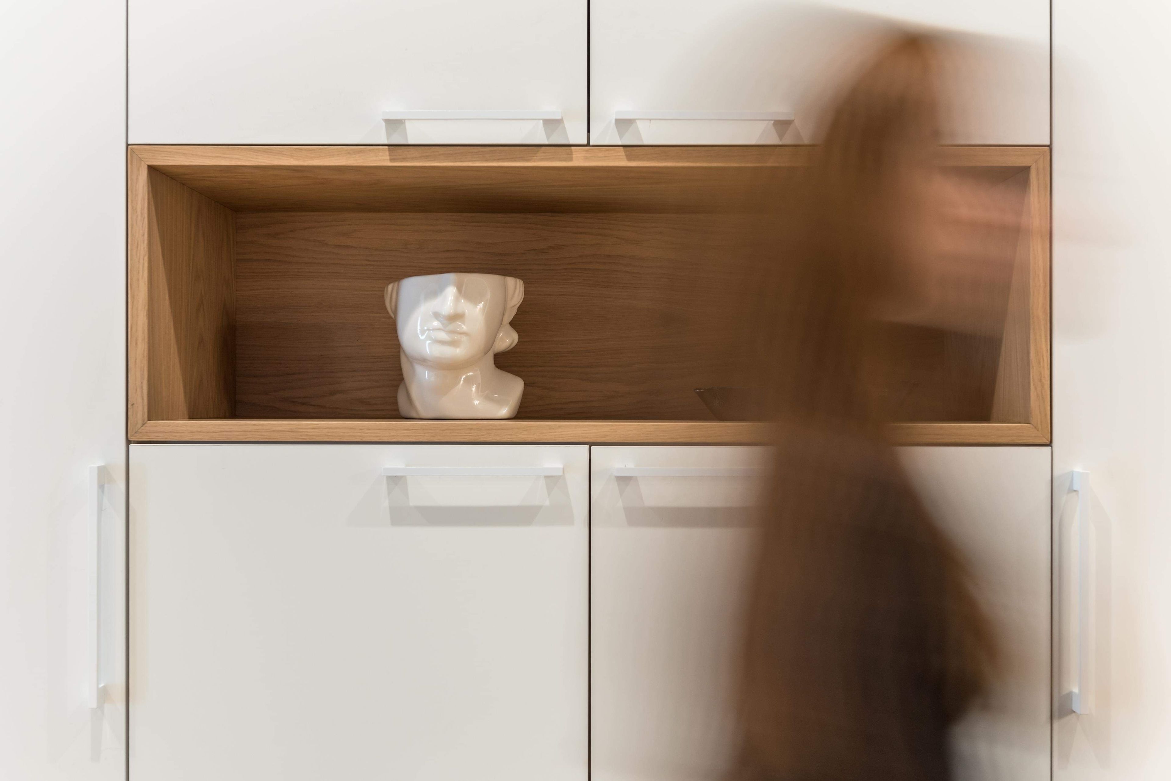 A white cabinet with a wooden shelf containing a bust sculpture.