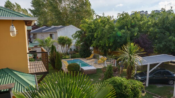 Patio trasero residencial con piscina, un toldo para coches y abundante vegetación.