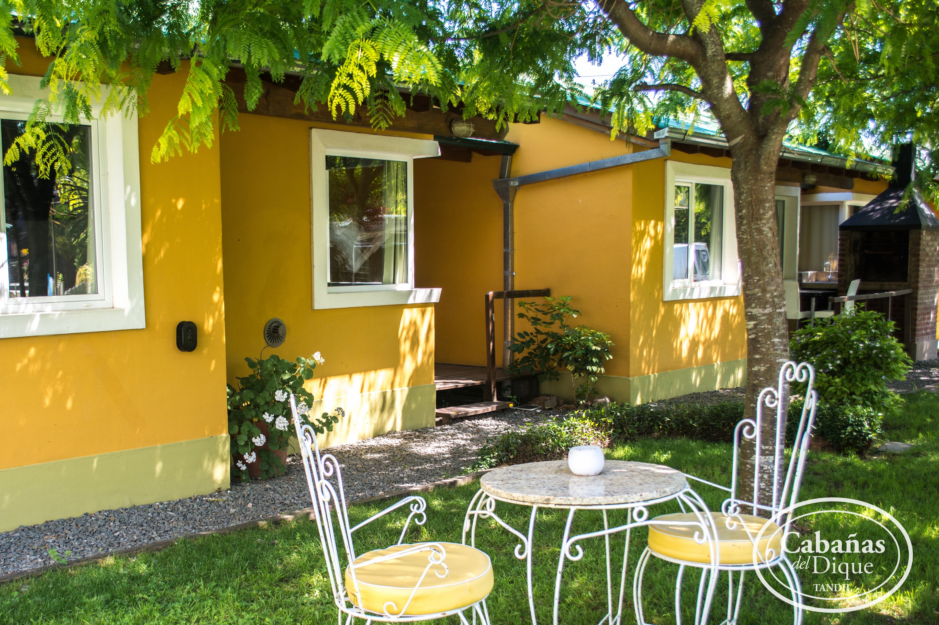 A yellow building with outdoor seating, a grill, and a tree providing shade.