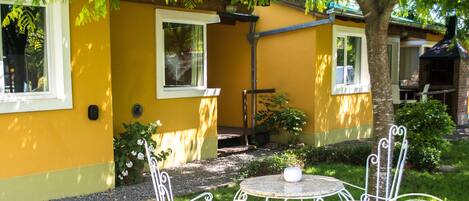 A yellow building with outdoor seating, a grill, and a tree providing shade.