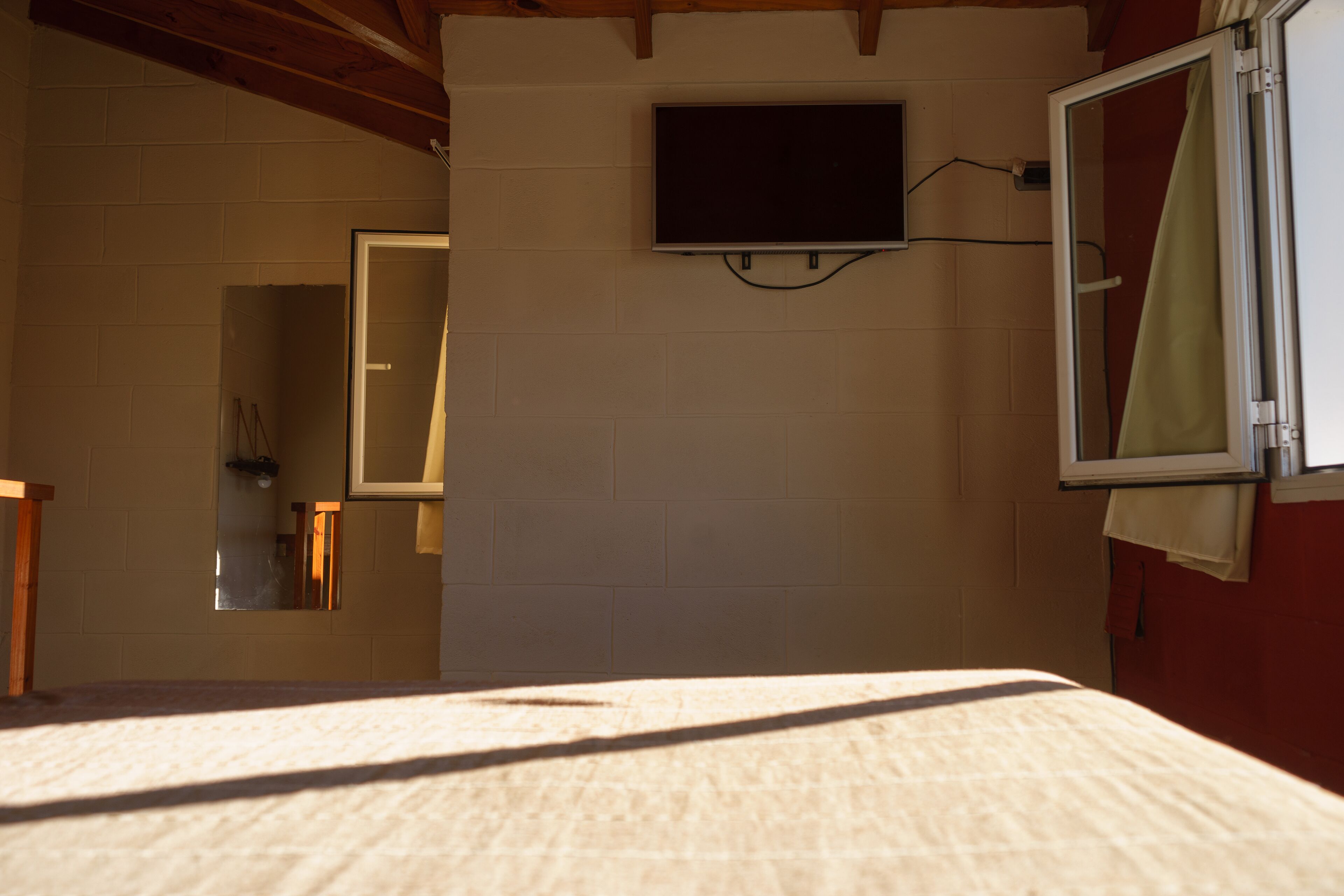 Een kamer met een bed, een aan de muur bevestigde televisie, een spiegel en een raam met gordijn.