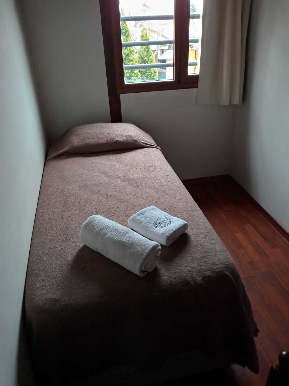 A small, neatly made bed with a brown bedspread and two white towels placed on it.