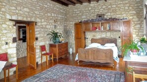 A rustic bedroom with a stone wall, wooden bed, and a red chair. - Maison les Beaux Arts (Mouzay)