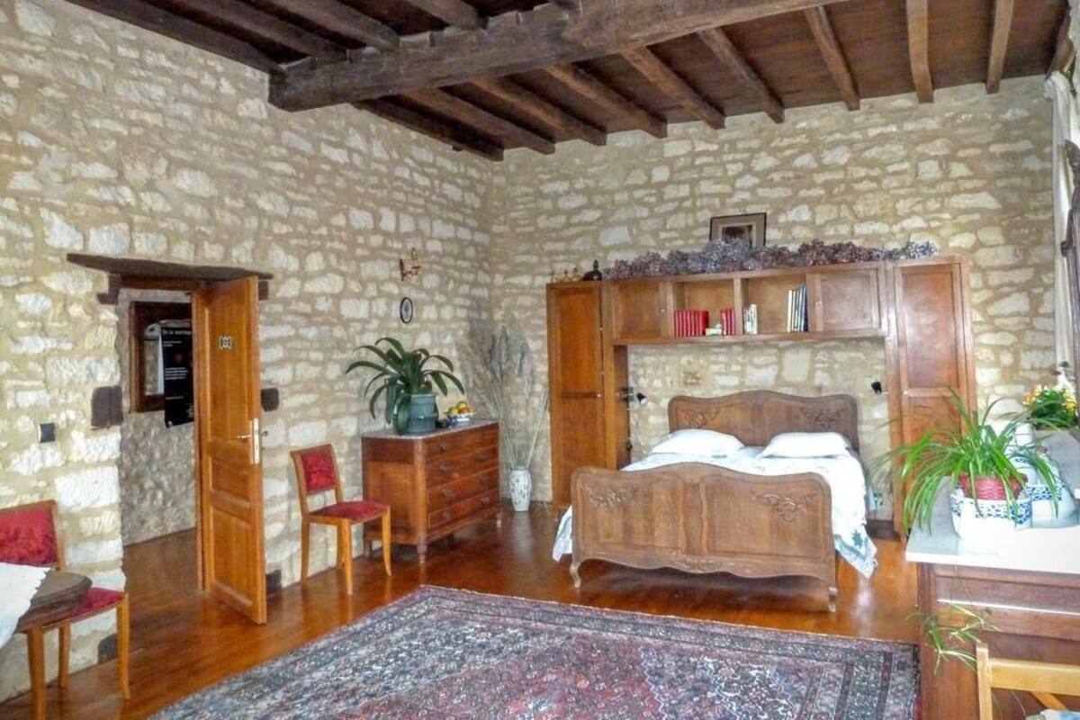 Un dormitorio rústico con pared de piedra, cama de madera y una silla roja.