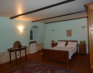 A bedroom with a wooden bed, a small table, a radiator, and a wall-mounted light fixture. - Maison les Beaux Arts (Mouzay)