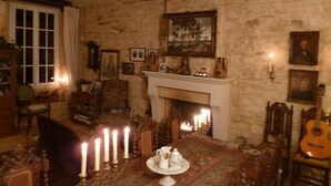 A cozy room with a fireplace, a dining table with candles, and various framed pictures on the walls. - Maison les Beaux Arts (Mouzay)