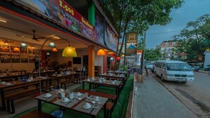 An outdoor dining area with multiple tables set for service, a sign for 'G-Z Plan B Hostel', and a white van parked on the street. - G&Z Plan B Hostel (Siem Reap)
