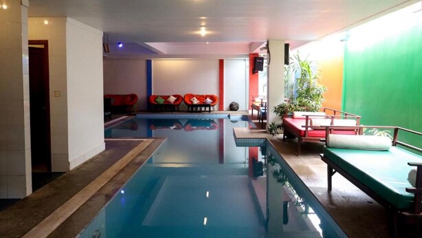 A swimming pool with a red and white seating area, a green wall, and a small table with a plant. - G&Z Plan B Hostel (Siem Reap)