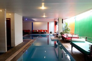 A swimming pool with a red and white seating area, a green wall, and a small table with a plant. - G&Z Plan B Hostel (Siem Reap)