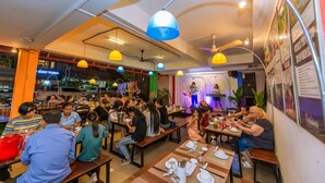 A restaurant with multiple dining tables and benches, a stage with a performer, and a sign for 'YUNA' in the background. - G&Z Plan B Hostel (Siem Reap)
