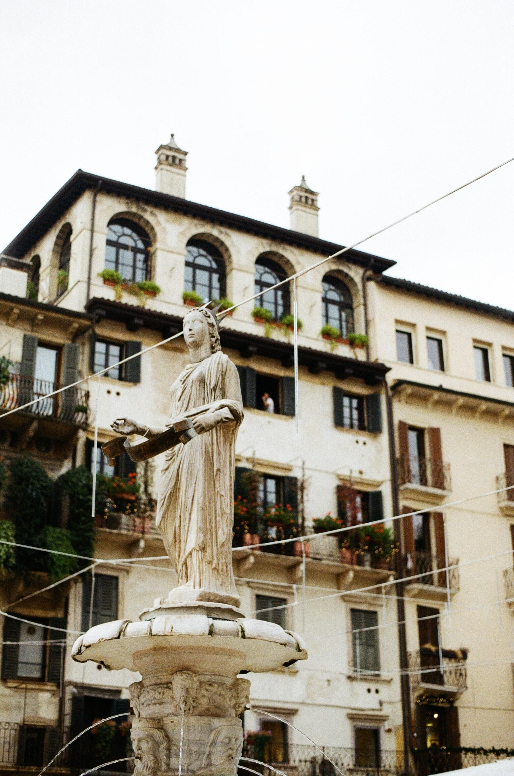 A statue on a pedestal with a fountain, set against a building with balconies and windows.