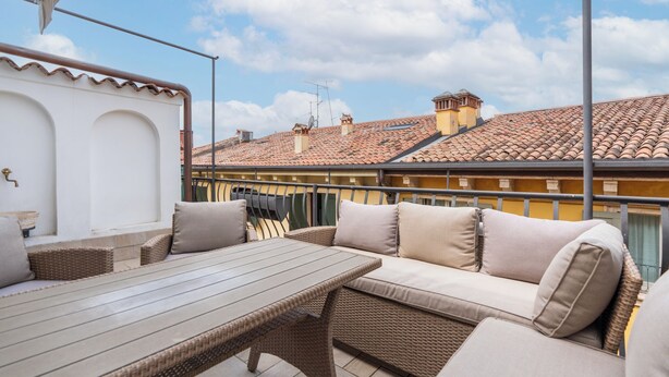 Eine Terrasse mit Korbmöbeln und einem Tisch, mit Blick auf eine Stadtlandschaft mit Terrakotta-Dächern.