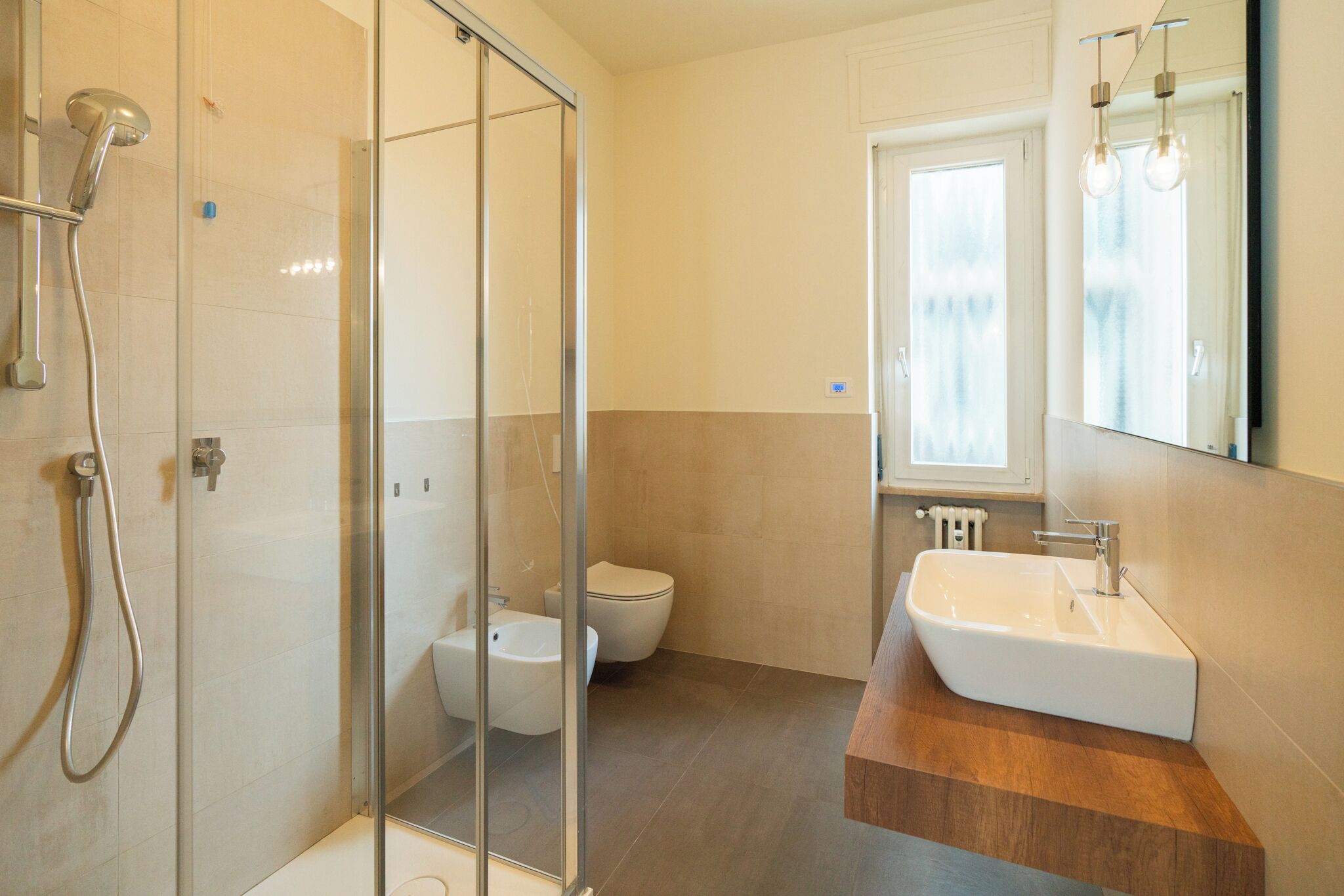 A modern bathroom with a glass shower enclosure, a toilet, and a sink with a wooden countertop.