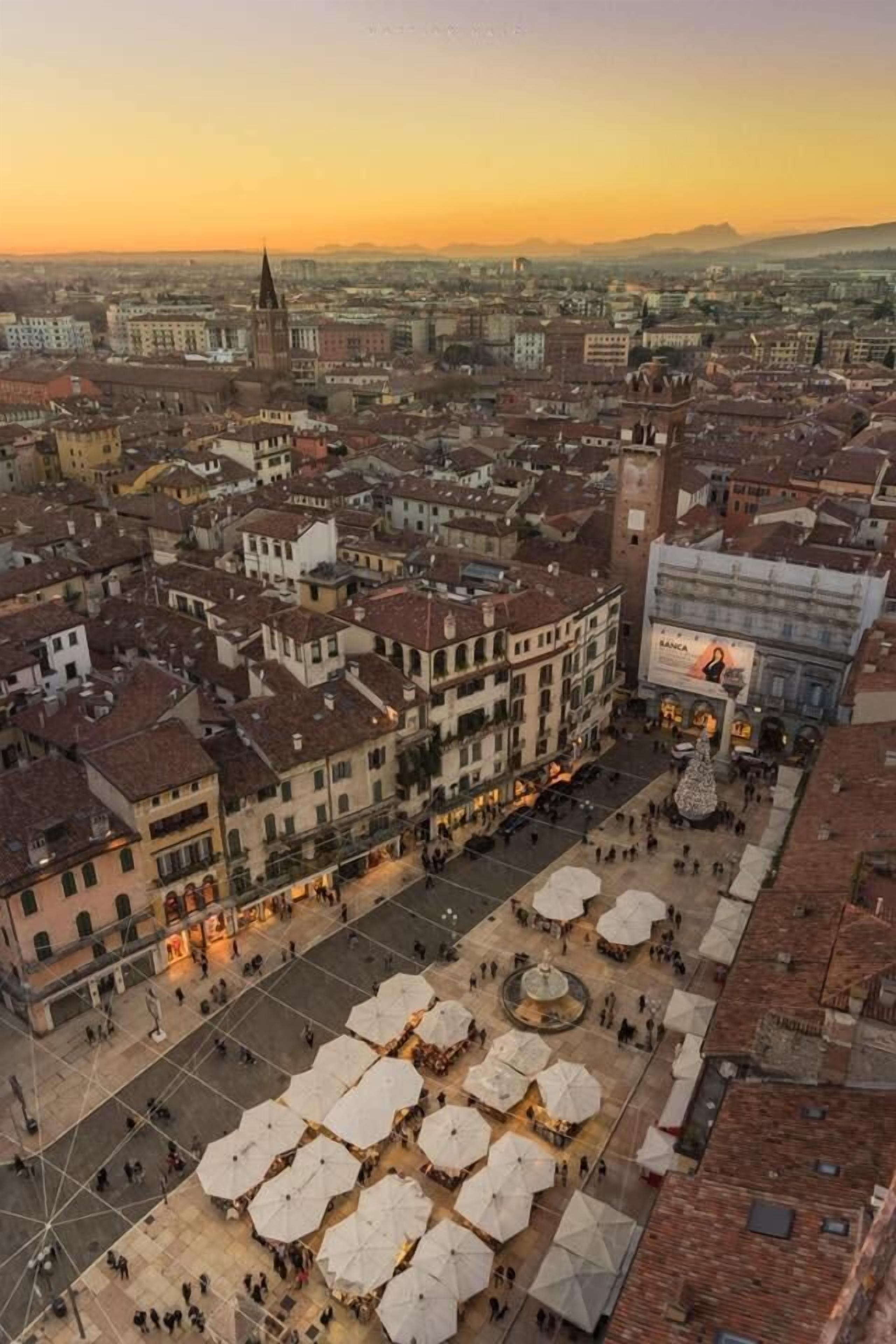 An aerial view of a city square with historic buildings, a prominent church spire, and a modern building with a billboard.