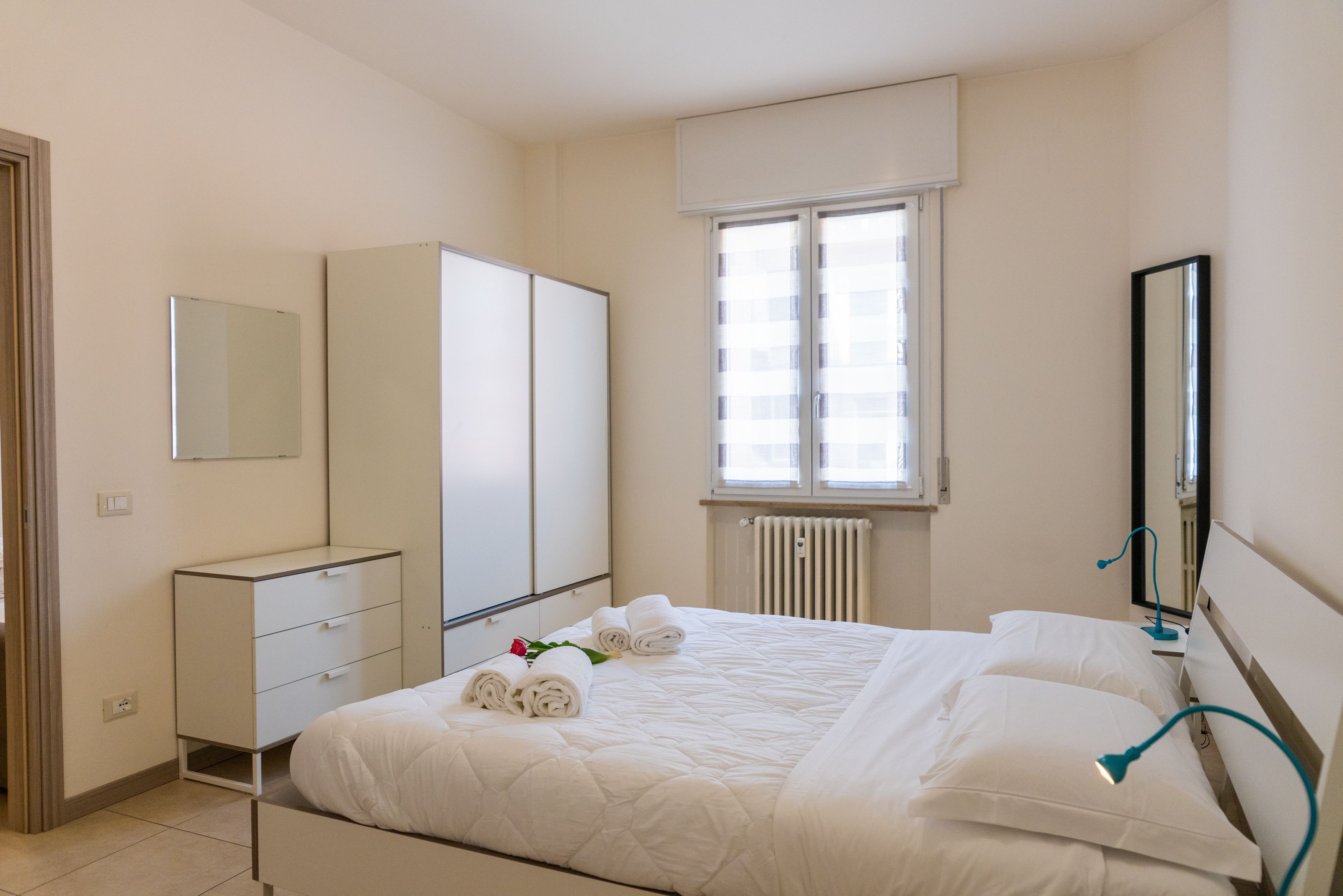Una habitación de hotel con cama, armario, ventana y espejo.