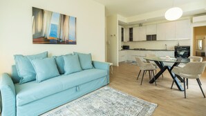 Ein modernes Wohnzimmer mit einem hellblauen Sofa, einem Esstisch mit Stühlen und einer Küche im Hintergrund.