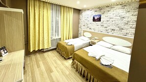 A hotel room with two beds, a wooden floor, a brick wall, and a window with curtains. - Grand Oral Hotel (Istanbul)