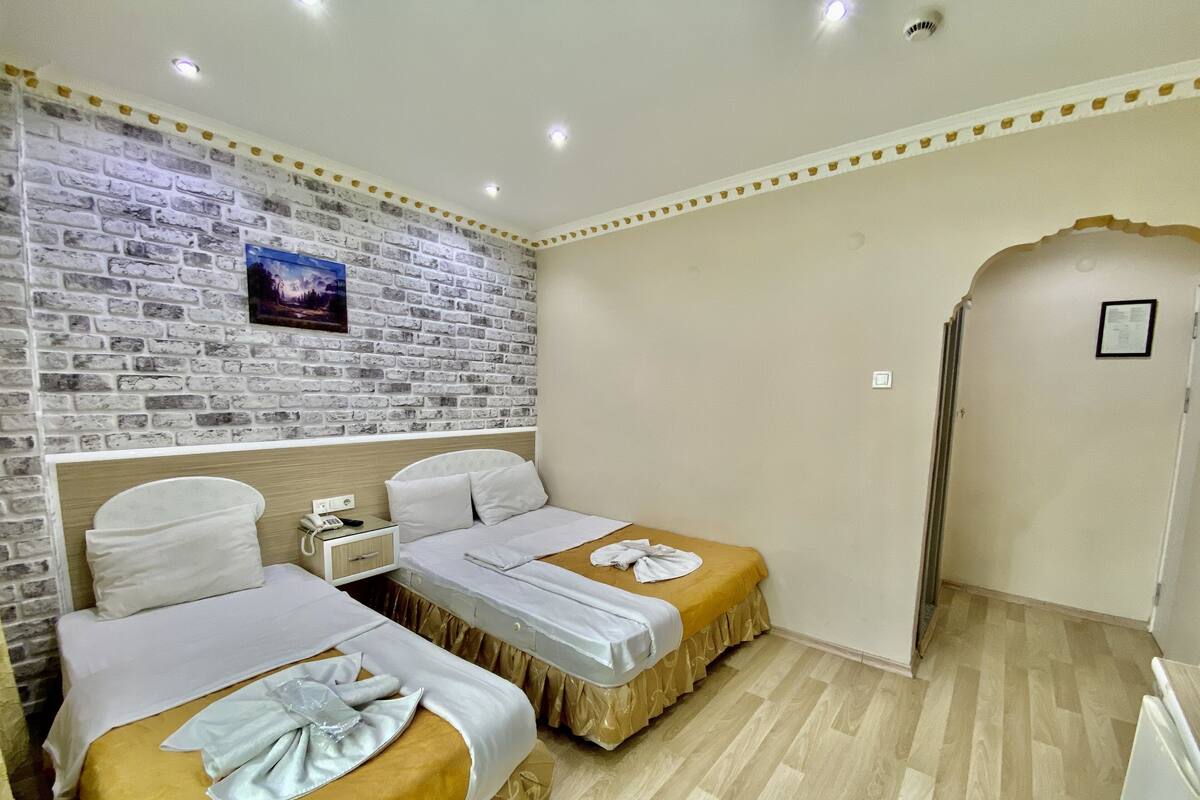 A hotel room with two beds, a brick-patterned wall, a wooden floor, and a small window.