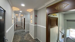 A hotel hallway with a carpeted floor, white walls, and a wooden door with a decorative design. - Grand Oral Hotel (Istanbul)