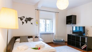 A neatly made bed with white linens and a bouquet of flowers, a black entertainment unit with a flat-screen TV, and a world map on the wall. - Τhe welcoming Rocchetto residence at 25m from P. Erbe (Verona)