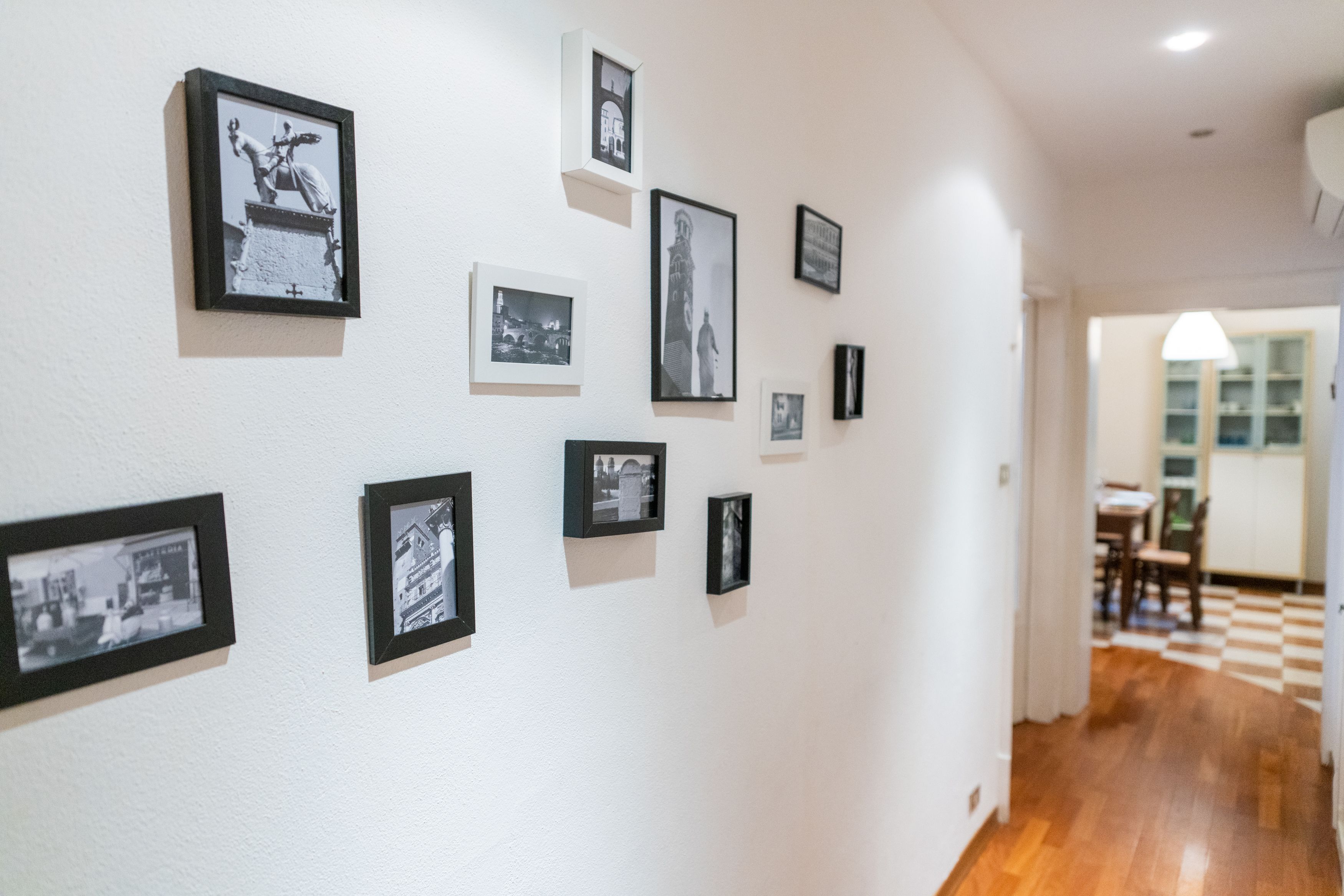 Un couloir orné de photographies en noir et blanc encadrées, qui mène à une salle à manger dont le sol est à carreaux.