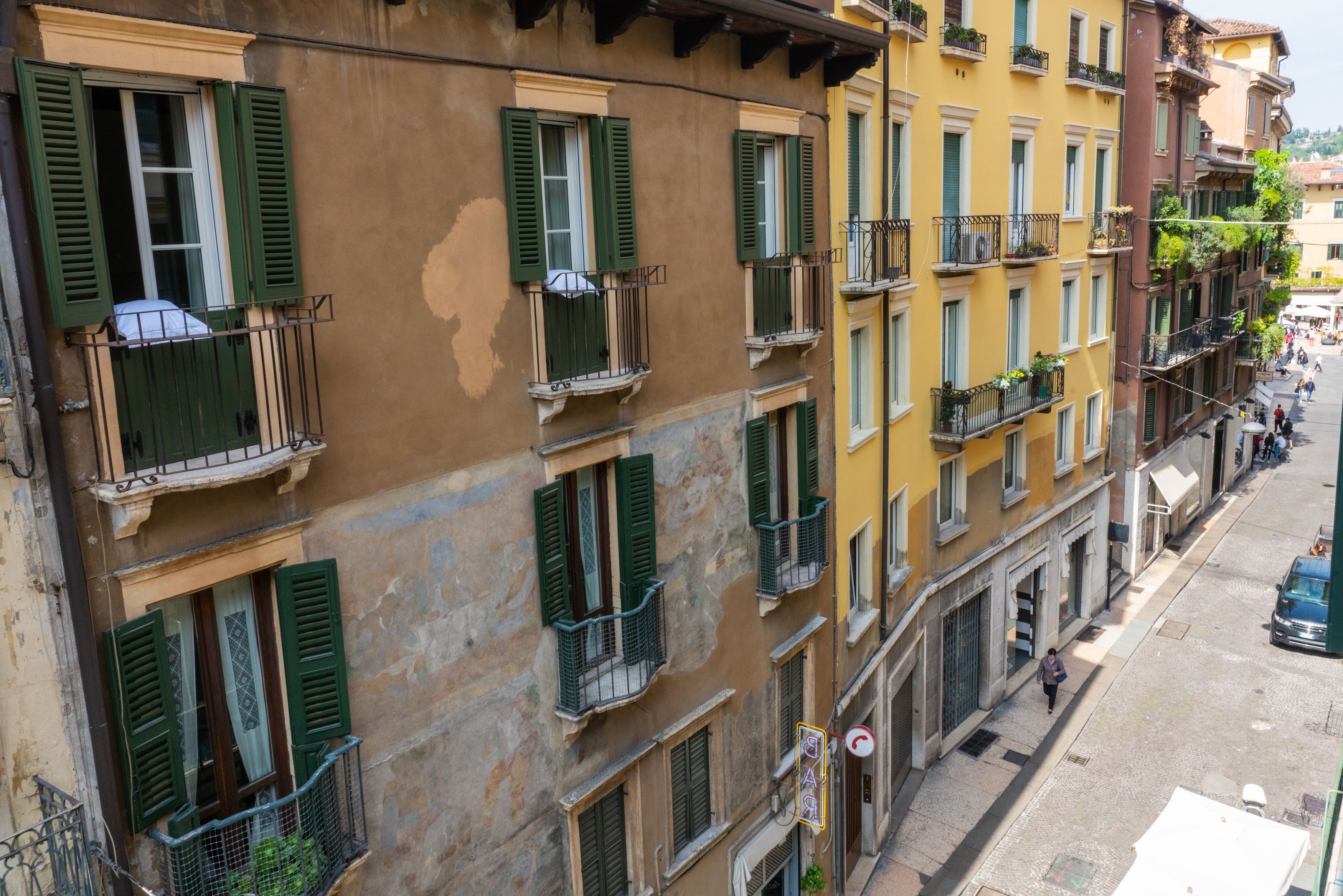 Un edificio a più piani con balconi, una strada antistante e un pedone.