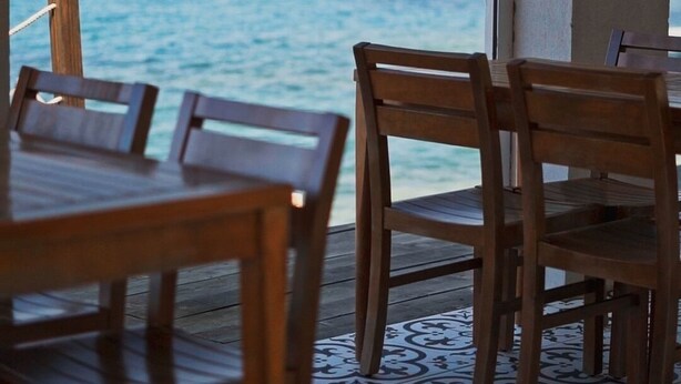 A dining area with wooden tables and chairs, a patterned floor, and a view of the sea through a large window. - Cunda Mira Butik Otel (Ayvalik)