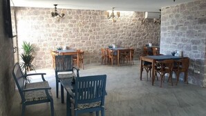 A stone-walled dining area with wooden tables and chairs, a potted plant, and a ceiling fan. - Cunda Mira Butik Otel (Ayvalik)